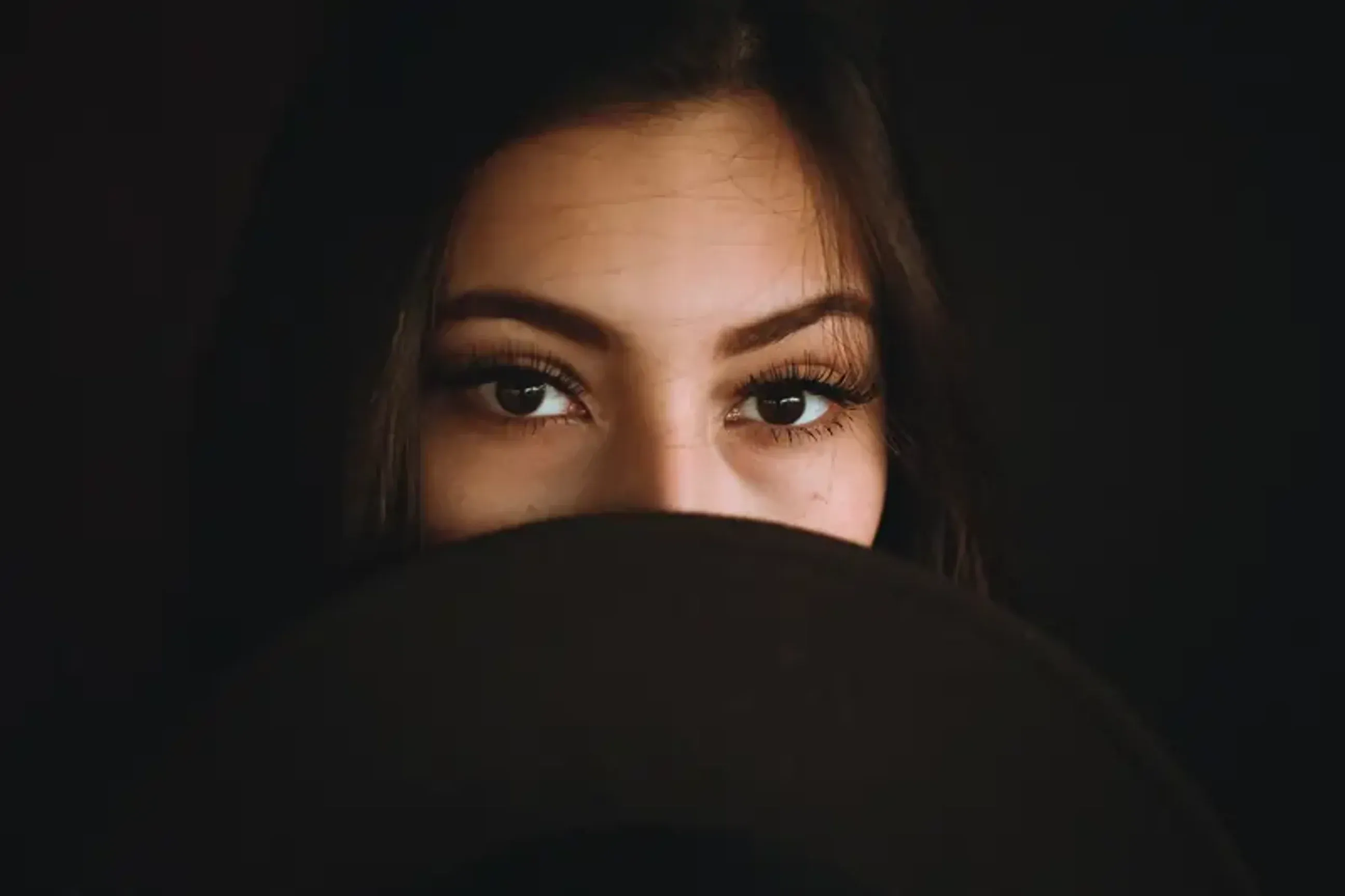 Close-up of woman’s eyes partially covered by dark fabric.